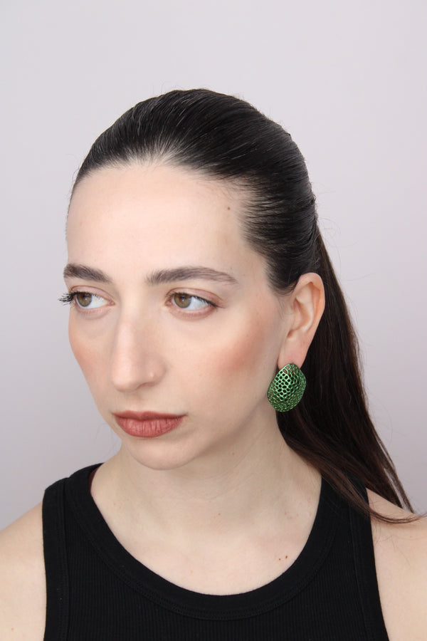 Woman wearing green earrings against a plain background