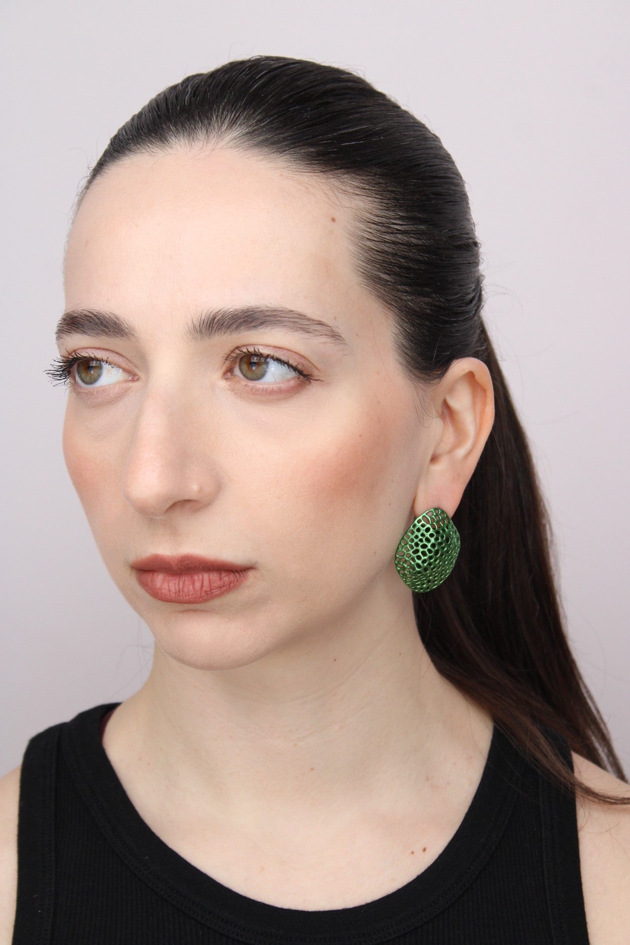 Woman wearing green earrings against a plain background