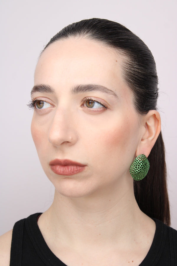 Woman wearing green earrings against a plain background