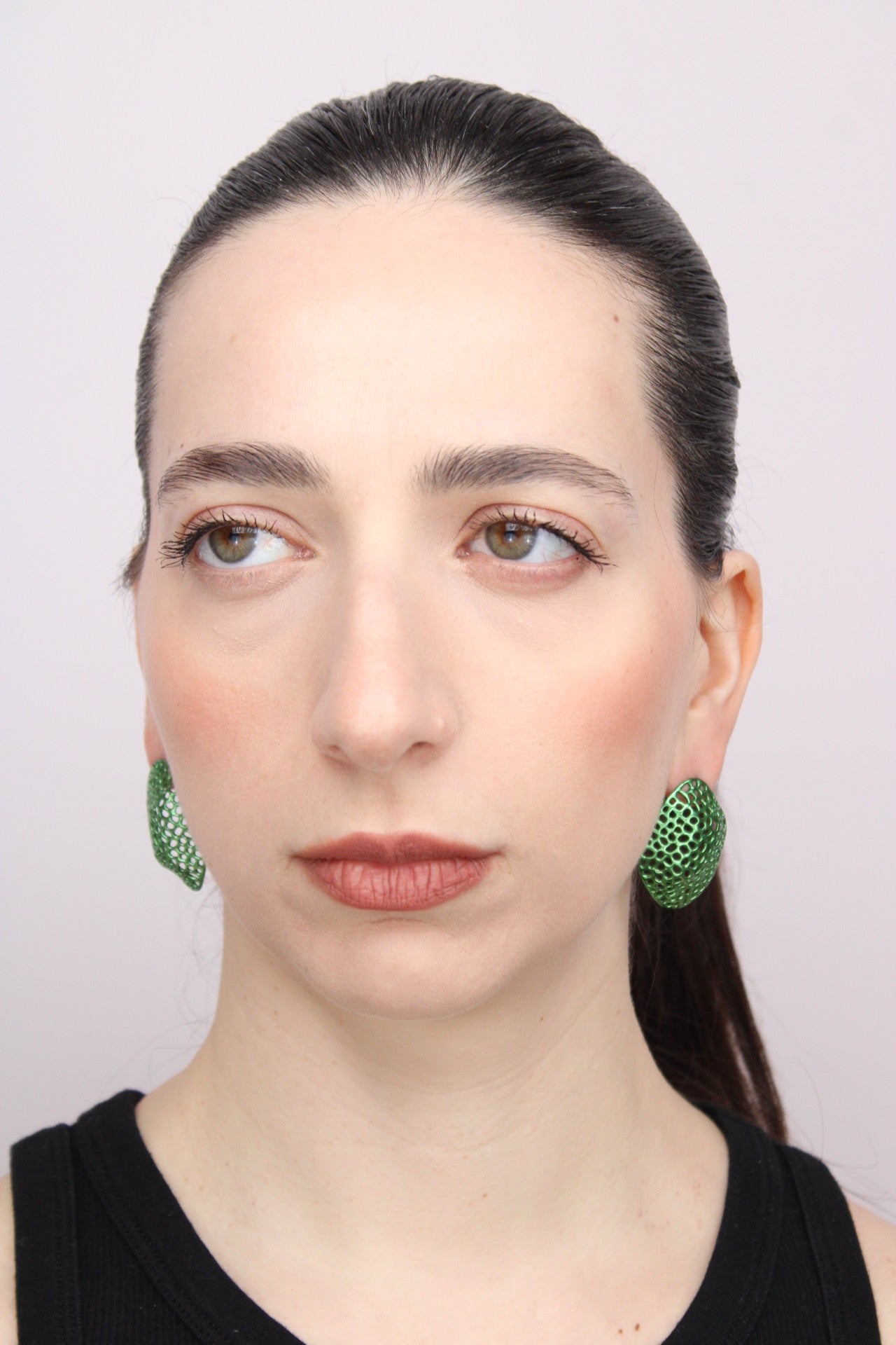 Woman wearing green earrings against a plain background