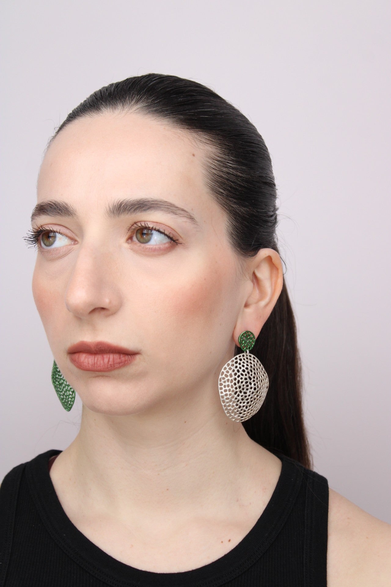 Woman wearing large, round earrings with a textured design on a plain background