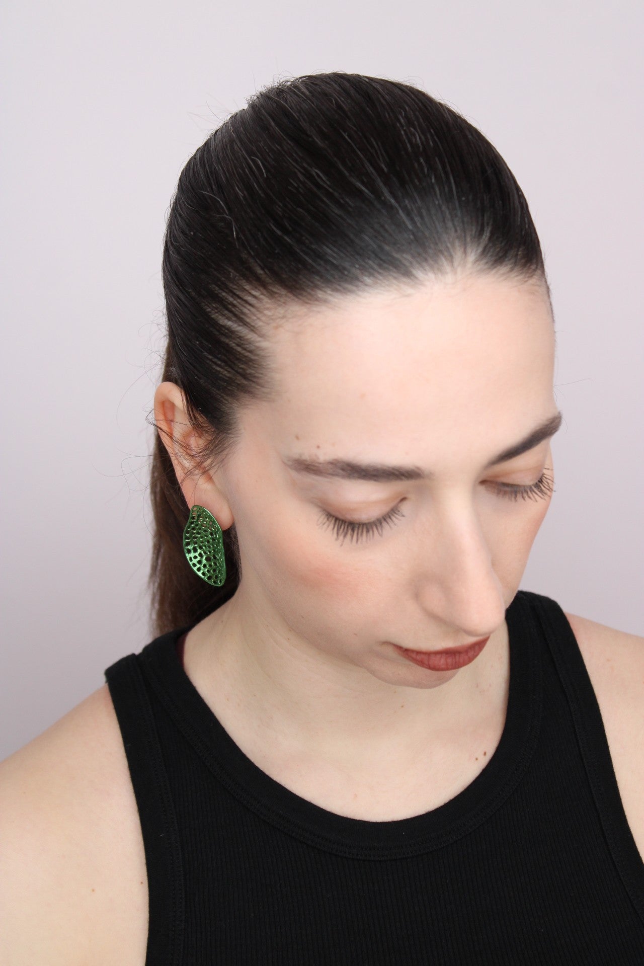 Woman wearing green earrings against a plain background