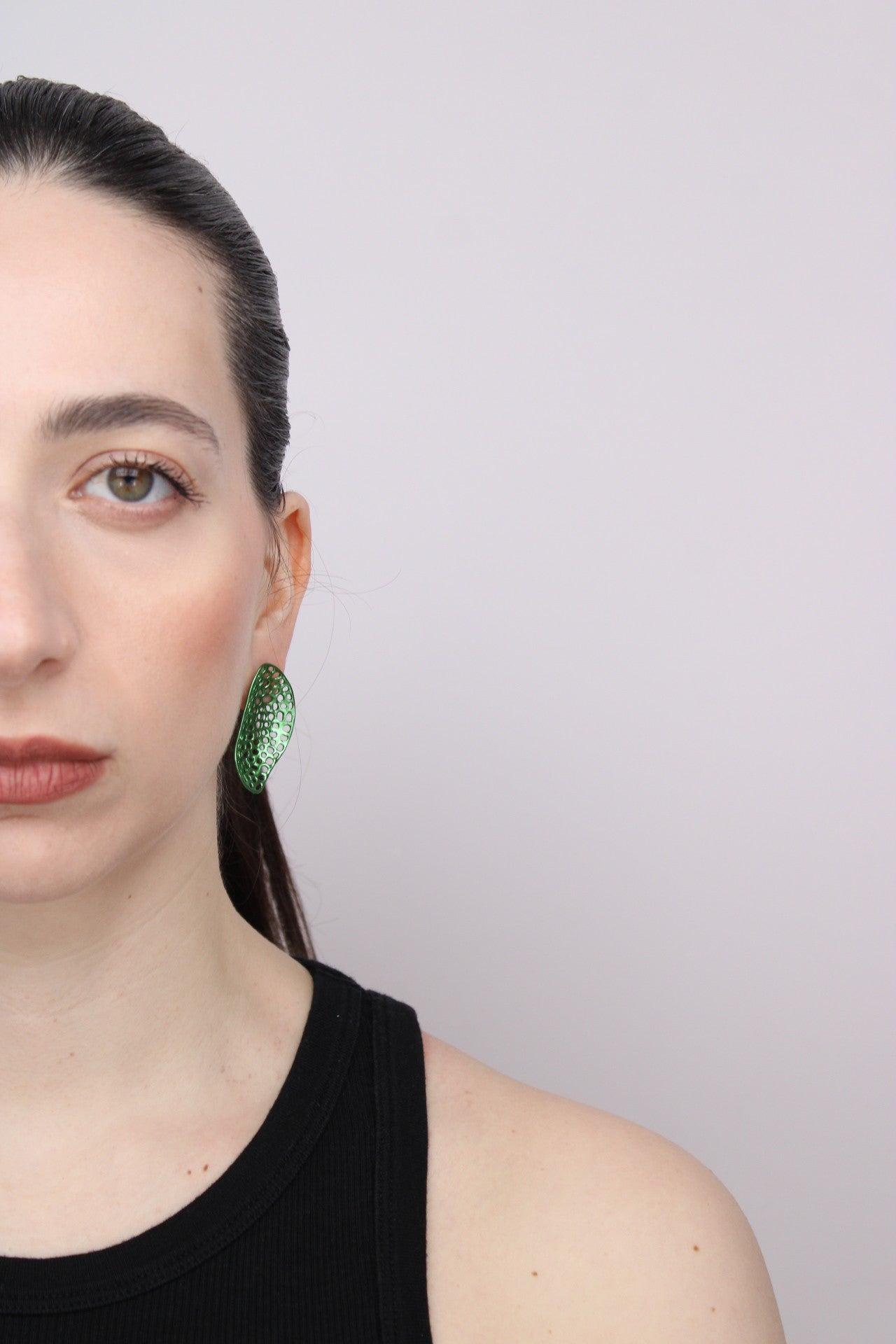Woman wearing green earrings against a plain background
