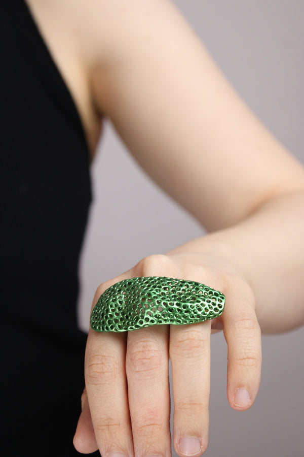 Hand wearing a green textured ring on a neutral background