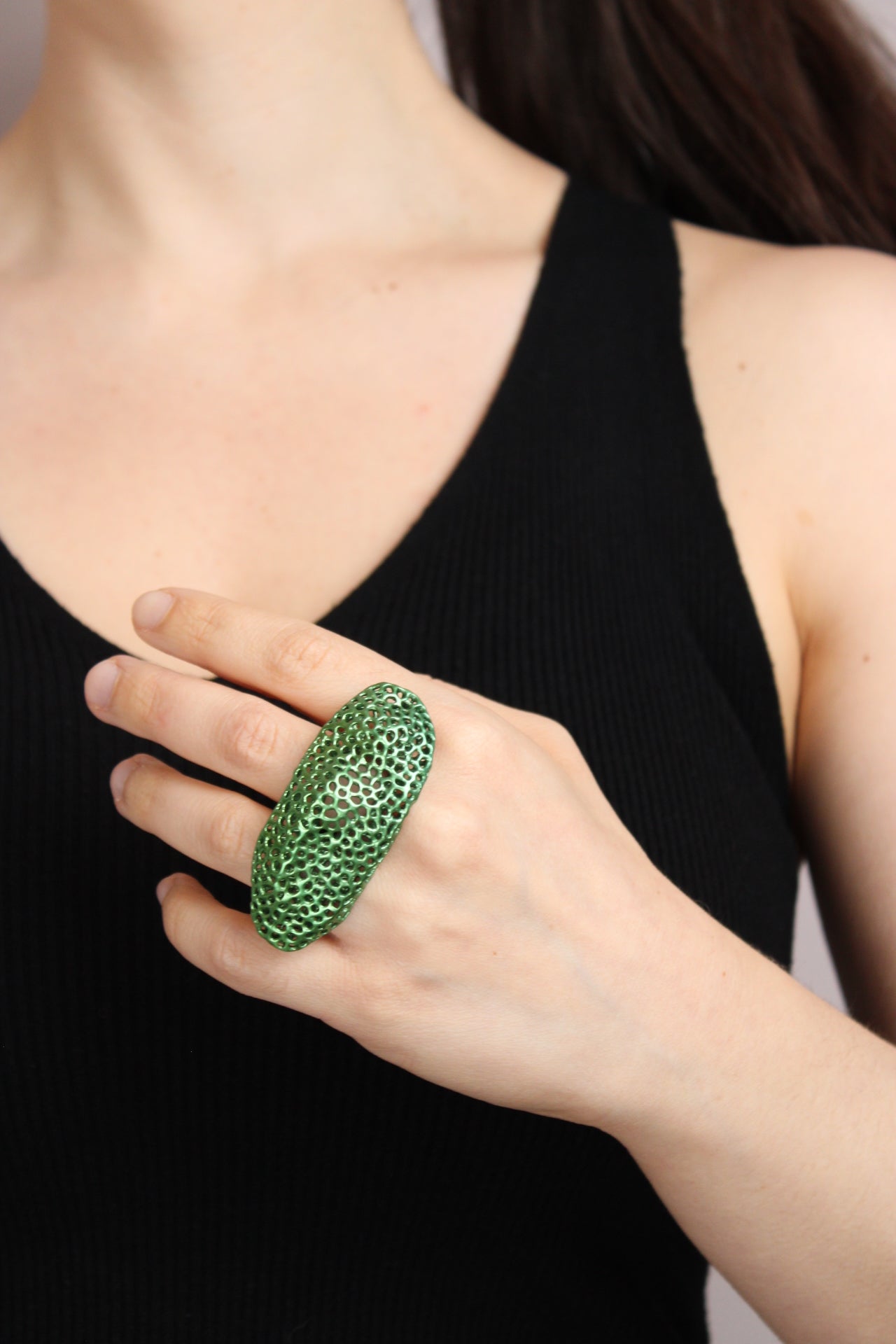 Person wearing a green textured ring on a black background