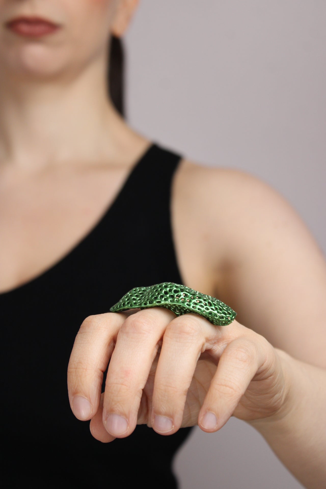 Close-up of a hand wearing a green textured ring on a neutral background