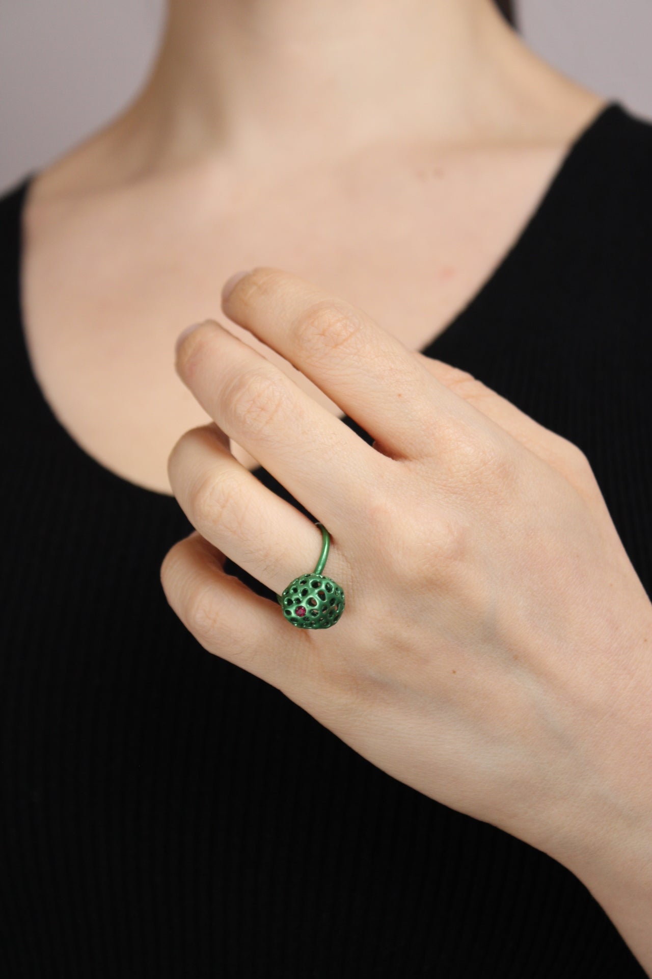 Hand wearing a green ring with a black background