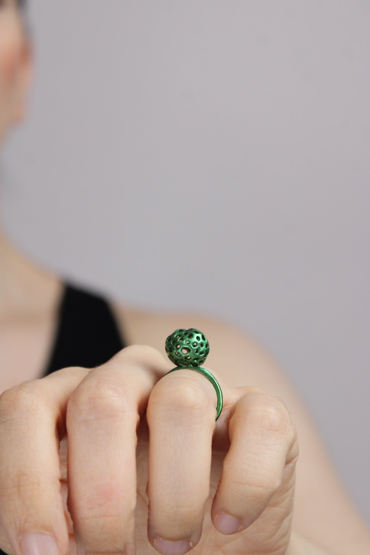 Hand wearing a green beaded ring on a gray background
