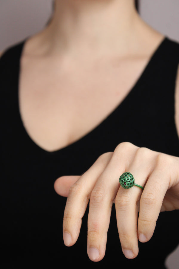 Close-up of a hand wearing a green ring on a blurred background