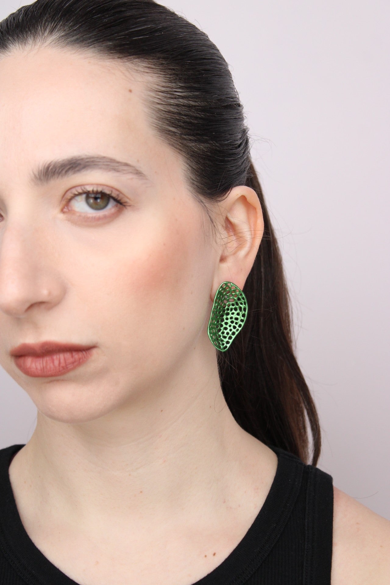 Woman wearing green an openwork leaf-shaped earrings against a plain background