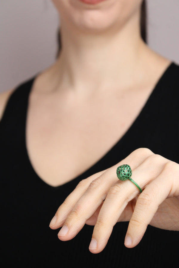 Hand wearing a green ring withb a small ruby against a black background