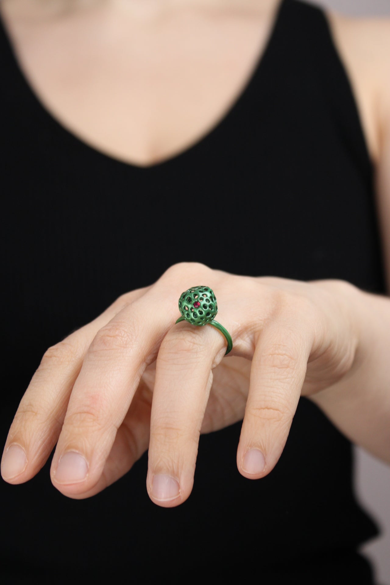 Hand wearing a green ring and one ruby with a black background