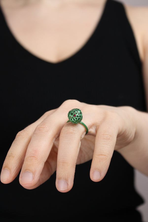 Hand wearing a green ring and one ruby with a black background