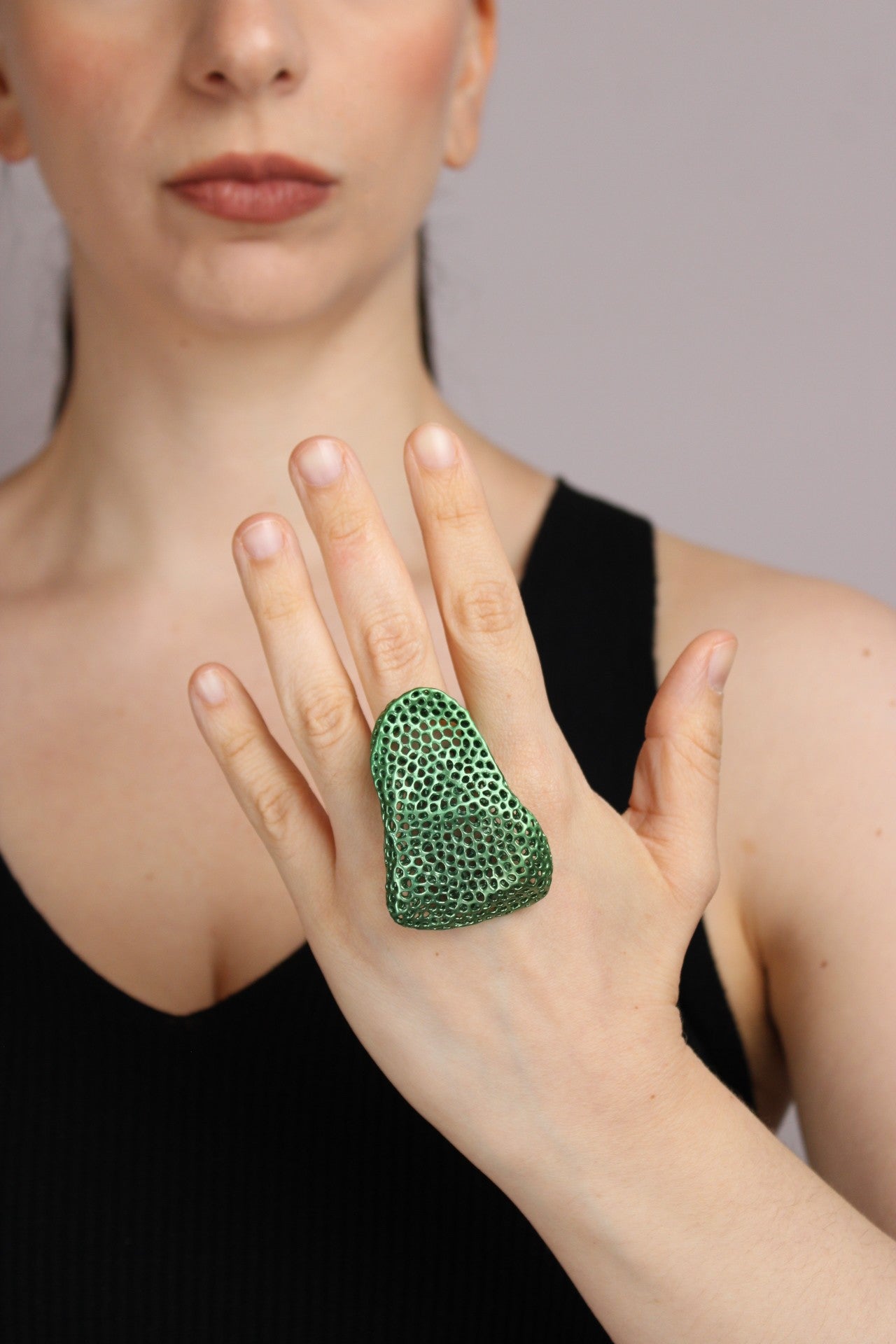 Woman wearing a green textured ring on her hand against a neutral background