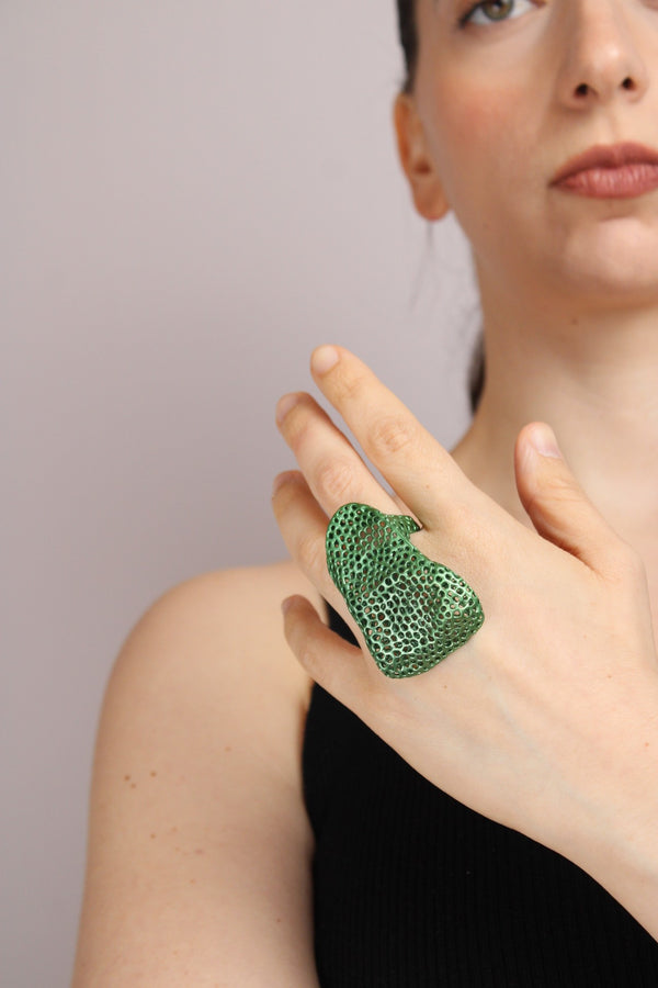 Woman wearing a green textured ring on a plain background