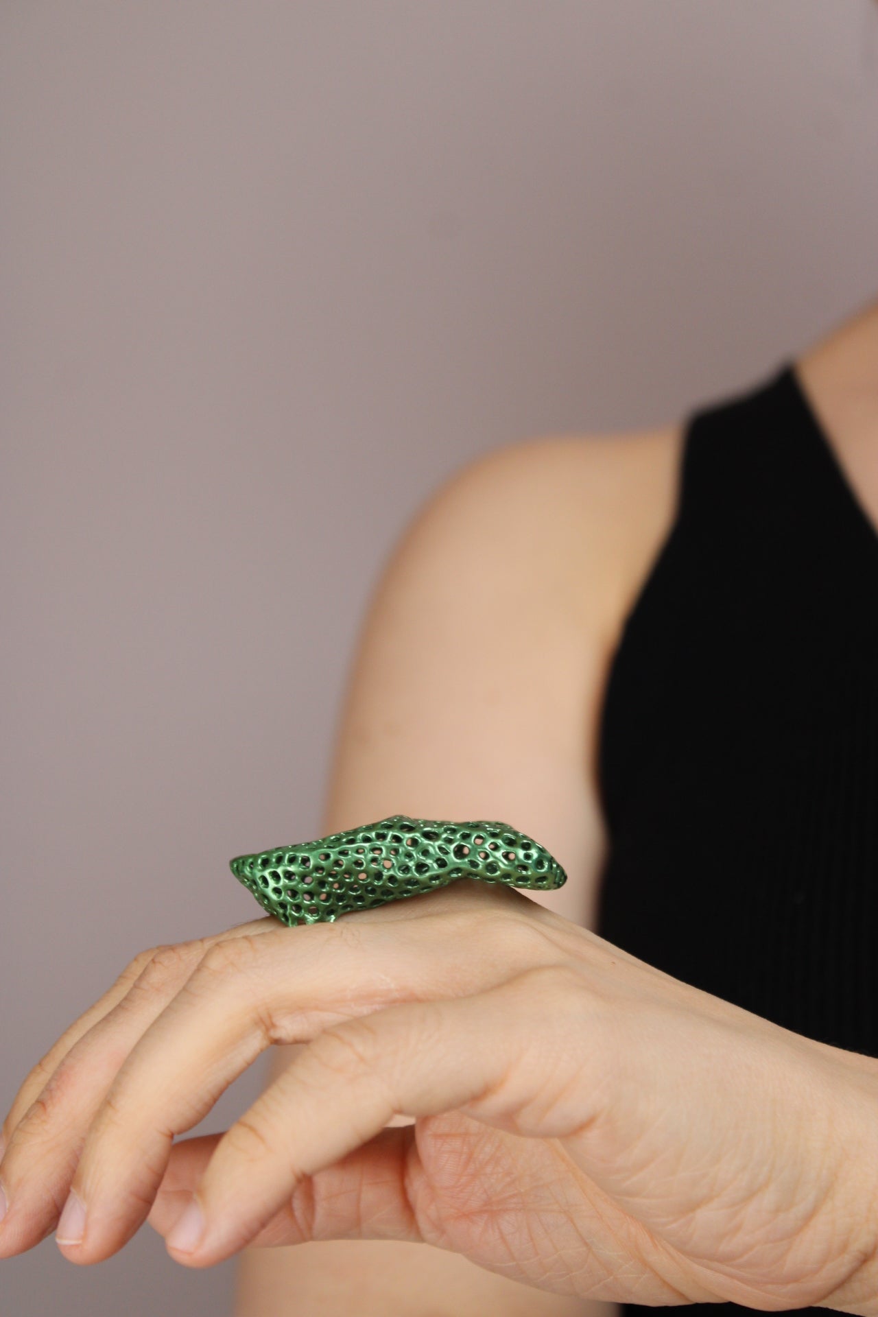Close-up of a hand wearing a green ring on a neutral background