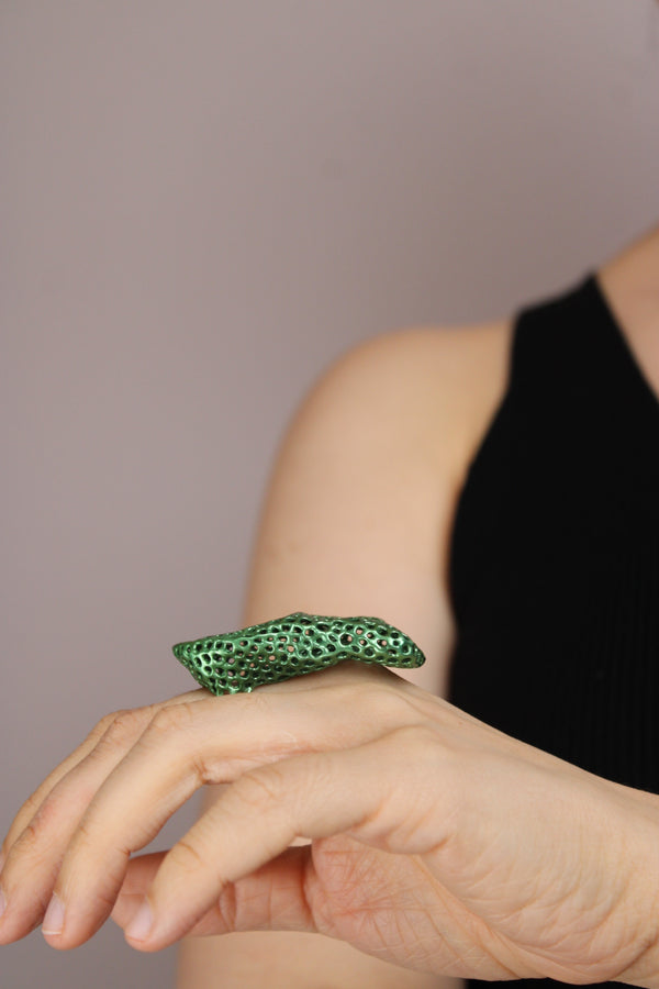 Close-up of a hand wearing a green ring on a neutral background
