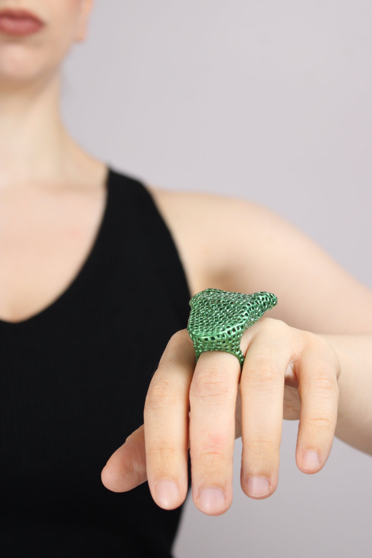 Hand wearing a green textured ring on a plain background