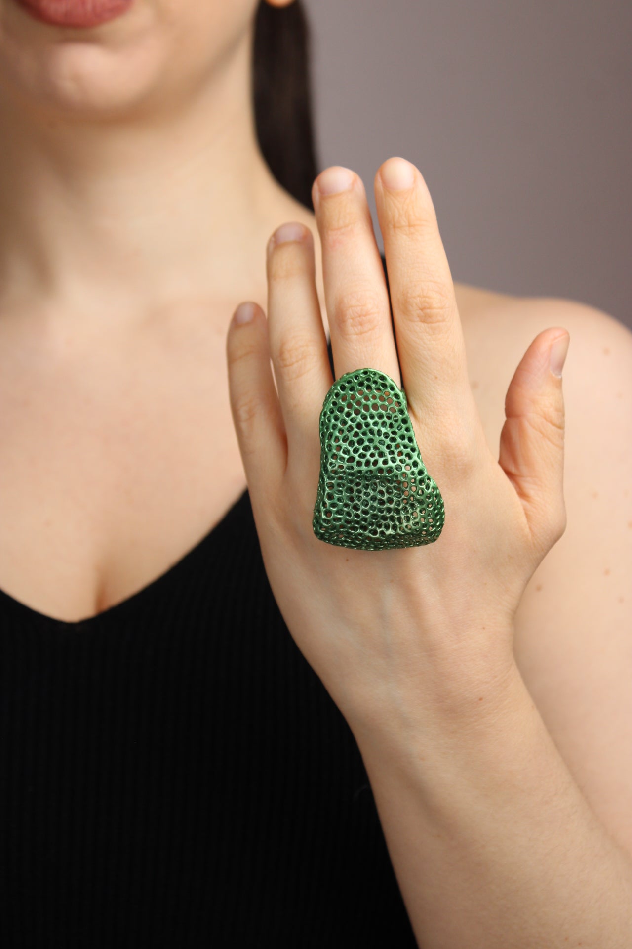 Close-up of a hand wearing a green ring with a textured design on a blurred background