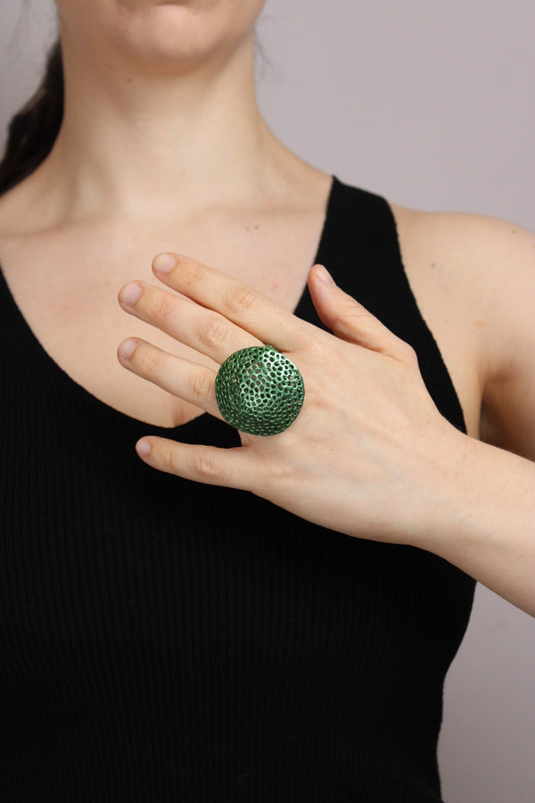 Person wearing a large green textured ring on a plain background