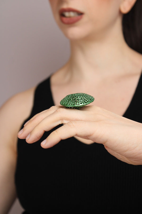 Person wearing a green textured ring on a plain background