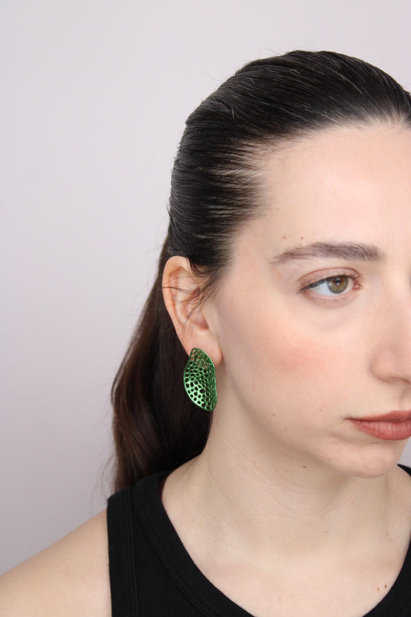 Woman wearing green earrings against a plain background