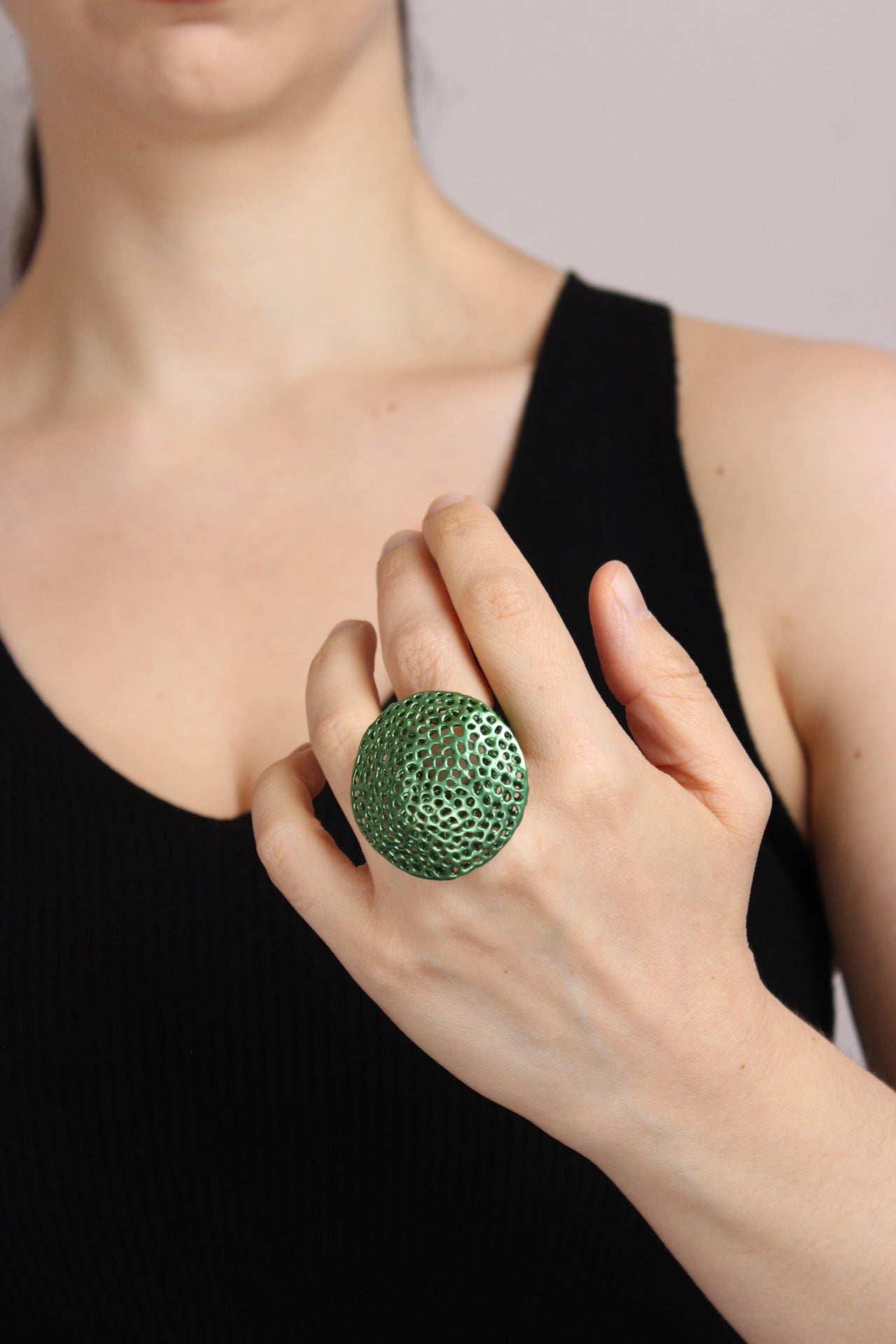 Person wearing a green textured ring on a neutral background