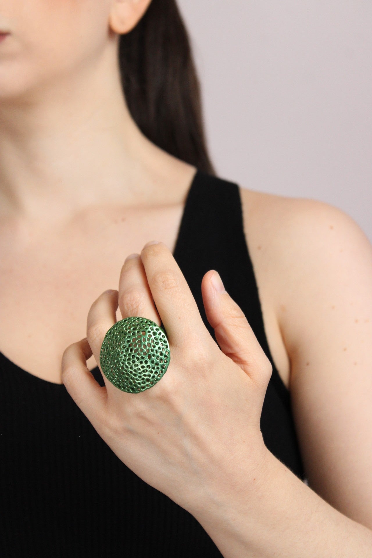 Person wearing a green textured ring on a plain background