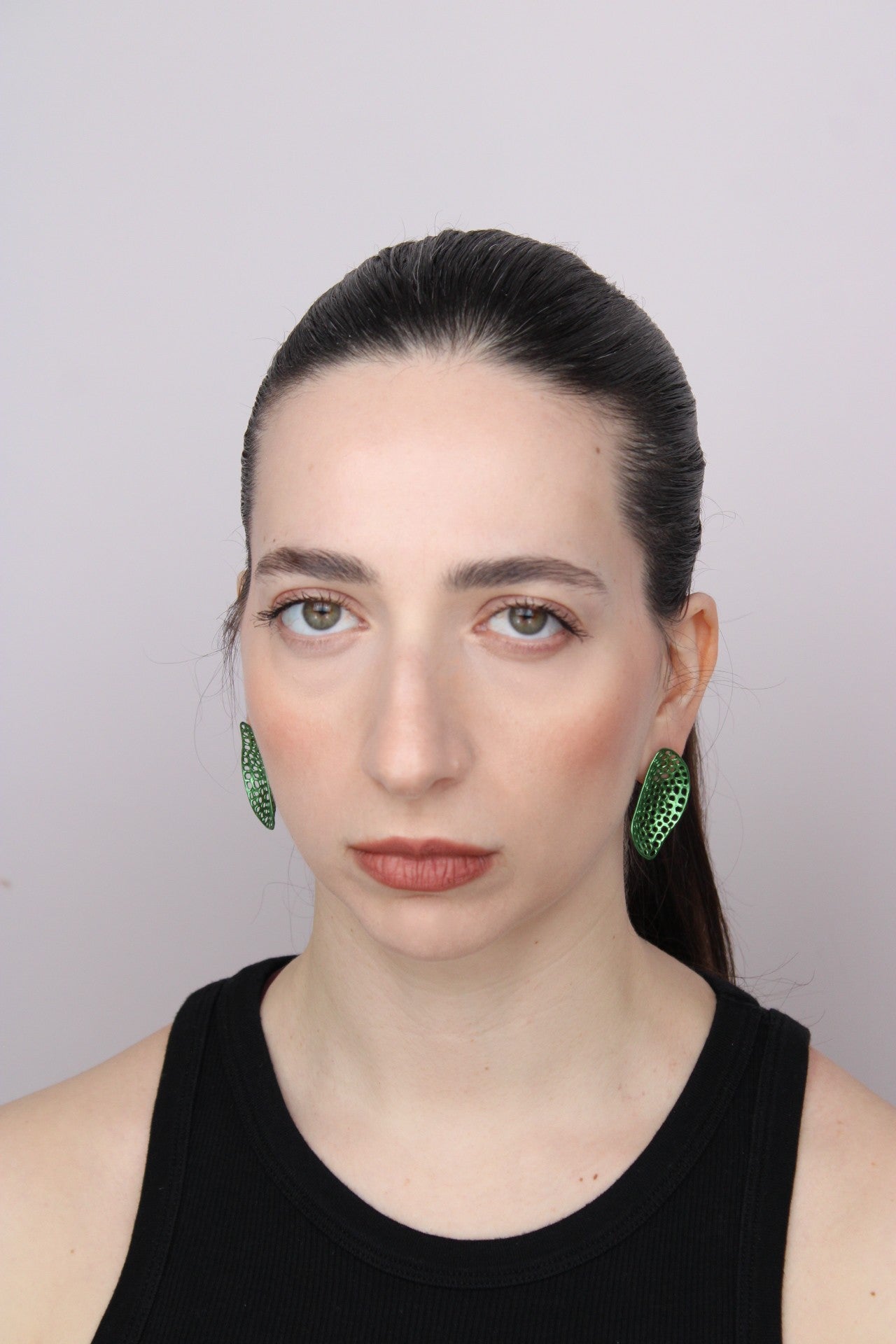 Woman wearing green earrings against a plain background