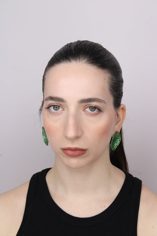 Woman wearing green earrings against a plain background